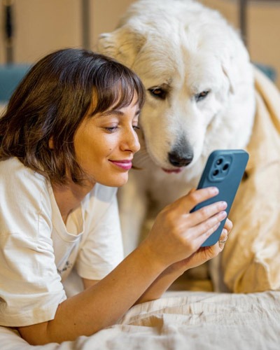 Woman using a blue phone beside a large white dog for pet care